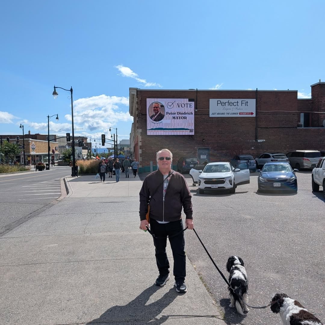 Peter Diedrich walking his dogs downtown in front of a Vote Peter Diedrich for Mayor billboard